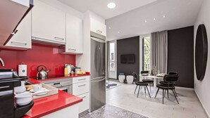 A modern kitchen with white cabinets and a red countertop, a dining area with a round table and chairs, and a large window with curtains.