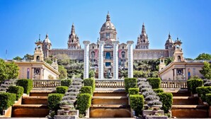 A grand building with multiple domes and towers, surrounded by well-manicured gardens and steps leading up to it.