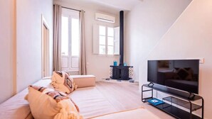 A modern living room with a sofa, a TV on a stand, a fireplace, and a window with curtains. - Sweett | Ethnic Eixample (Barcelona)