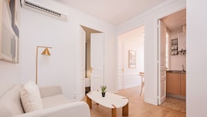 Una sala moderna con un sofá, una mesa de centro y una lámpara. Hay una puerta que conduce a una cocina y otra habitación.