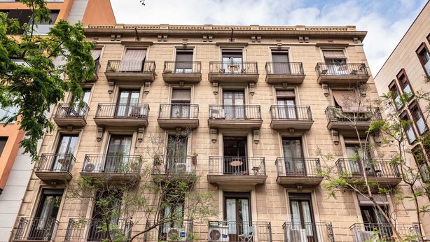 Un edificio de varios pisos con balcones, ventanas y algo de vegetación.