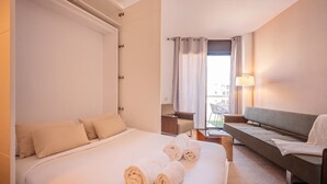 A hotel room with a bed, a sofa, a small table, and a lamp. - Sweett | Cosy Ciutadella (Barcelona)