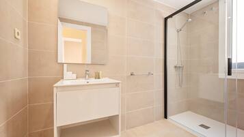 Un baño moderno con cabina de ducha de vidrio, tocador blanco y un espejo grande.