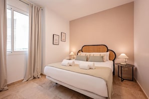 Une chambre à coucher avec un lit, deux tables de chevet, une fenêtre avec des rideaux et deux tableaux encadrés accrochés au mur.