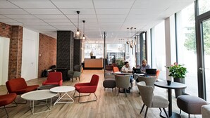 A modern lounge area with seating, a reception desk, and large windows. - B&B Hotel Zürich East Wallisellen (Wallisellen)