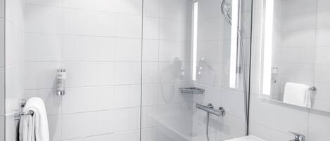 A modern bathroom with white tiles, a glass shower enclosure, a handheld showerhead, a handheld showerhead, a glass-enclosed mirror, and a white sink with a chrome faucet.