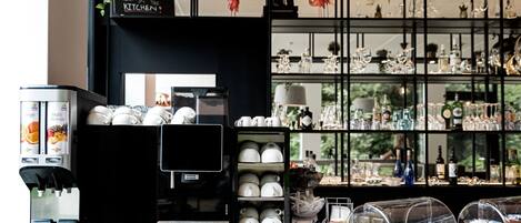 Una cafetera, una presentación de tazas blancas y una colección de vasos en un café.