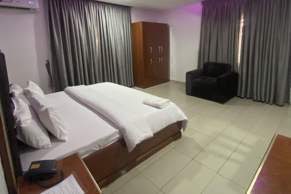 Une chambre d’hôtel comprenant un lit, un bureau avec un téléphone et des documents, une armoire, une chaise et des rideaux.