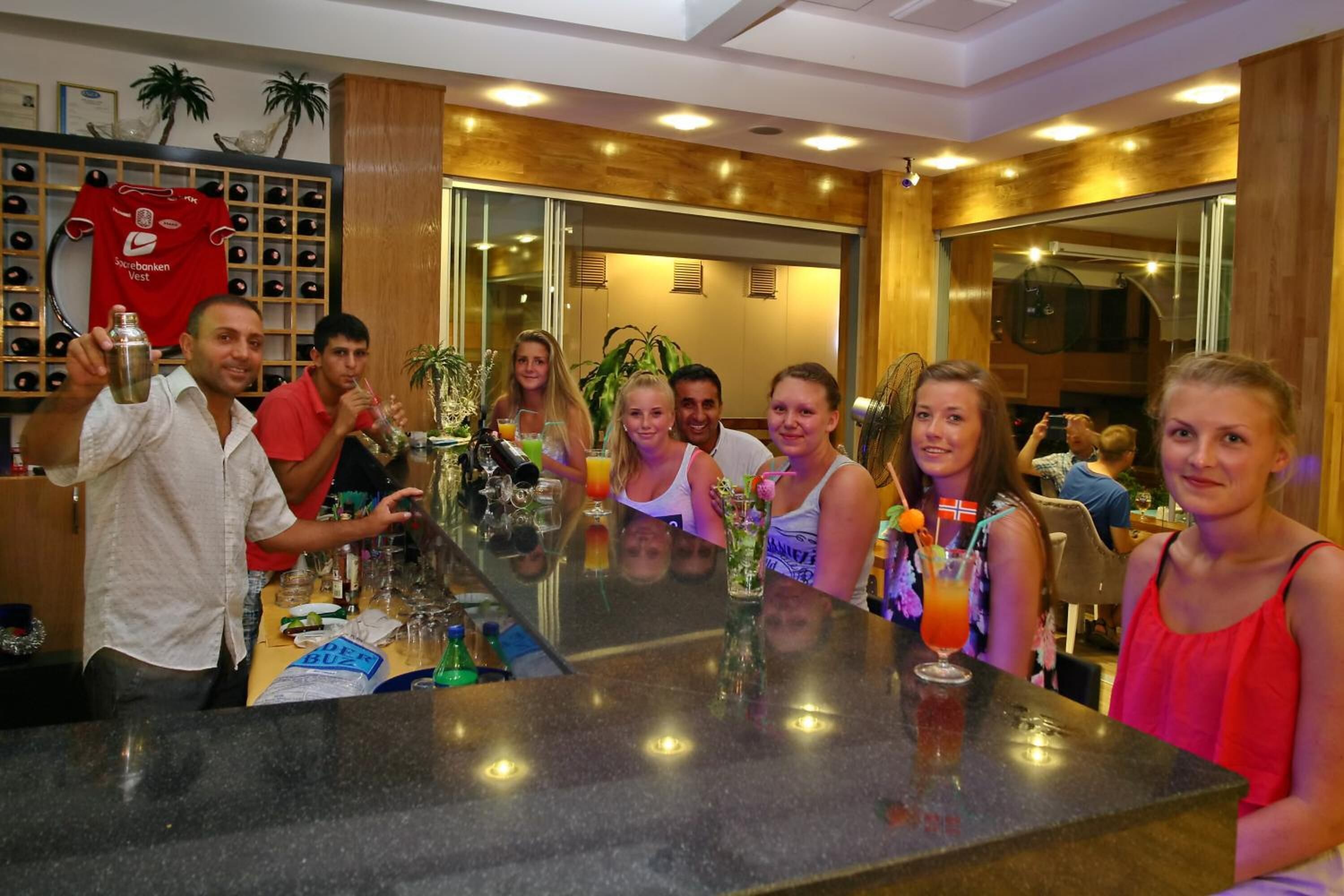A bar area with a long counter, various drinks, and a red sports jersey on the wall.