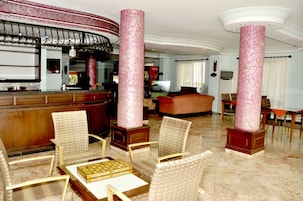 A spacious lobby with high ceilings, a reception desk, and several seating areas with wicker chairs and a sofa.