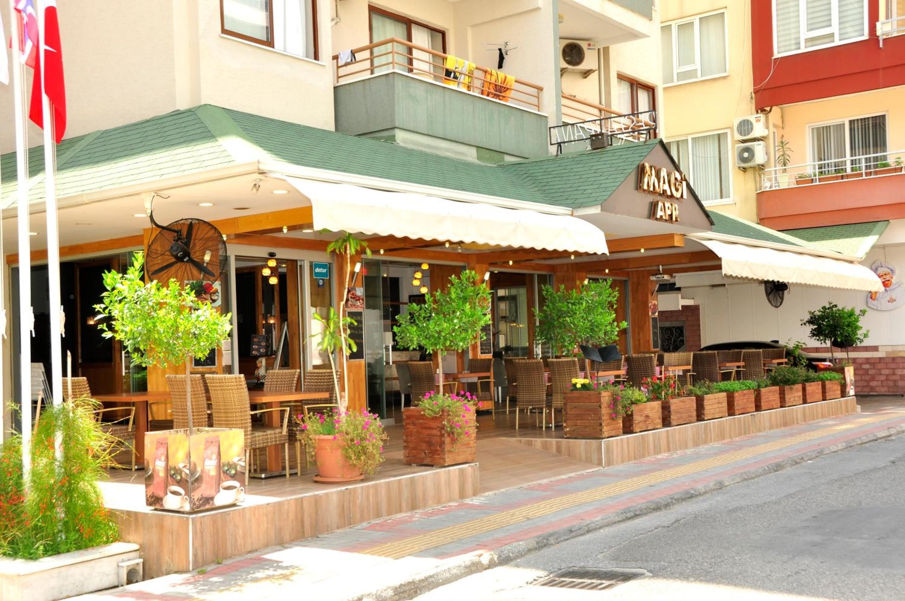 A restaurant with outdoor seating, a clock, and potted plants.
