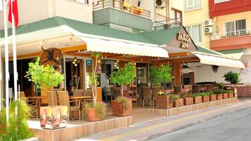 A restaurant with outdoor seating, a clock, and potted plants.