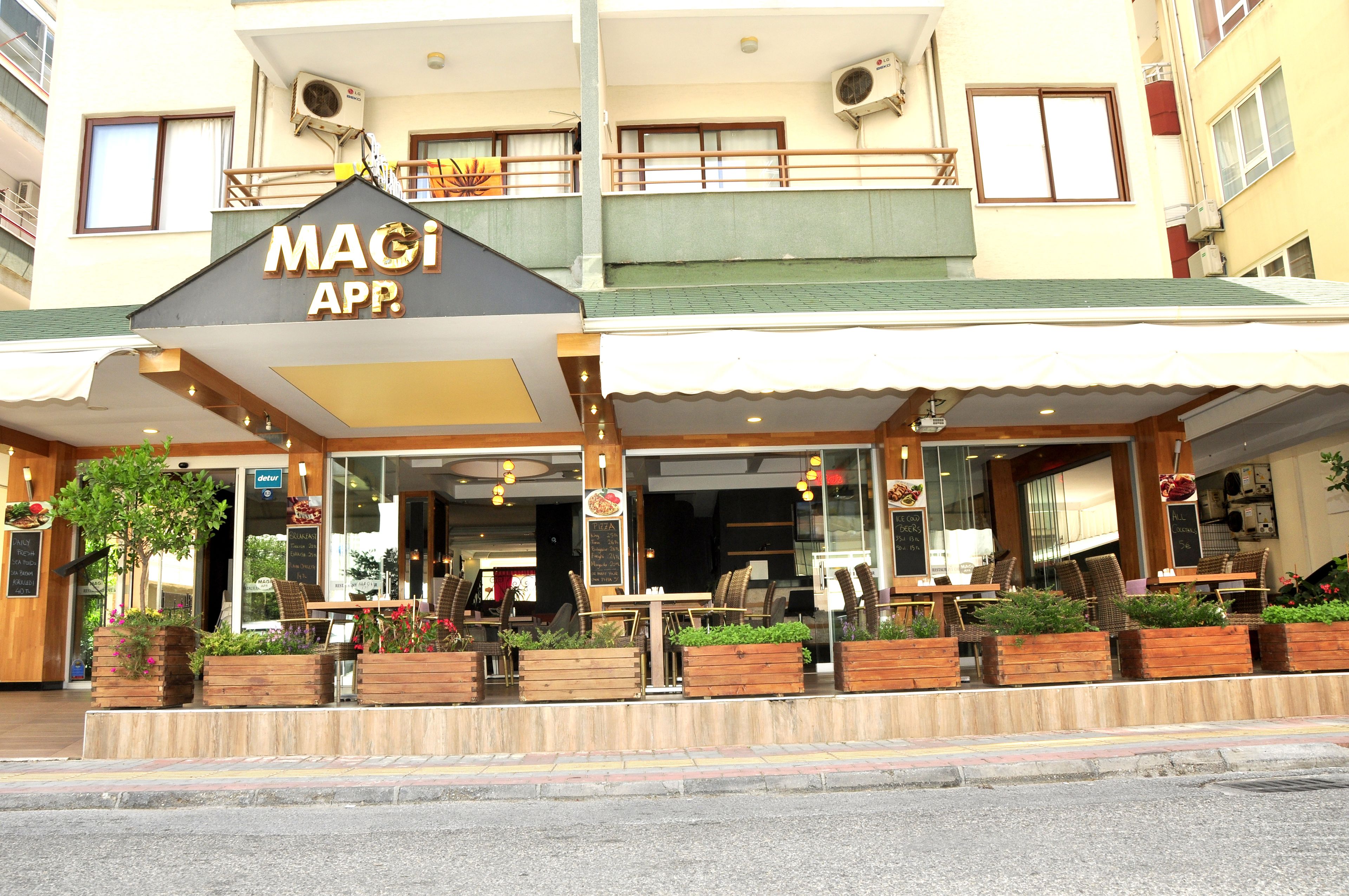 Een restaurant met terras, een bord waarop 'MAGI APP' staat, en een balkon met leuning.