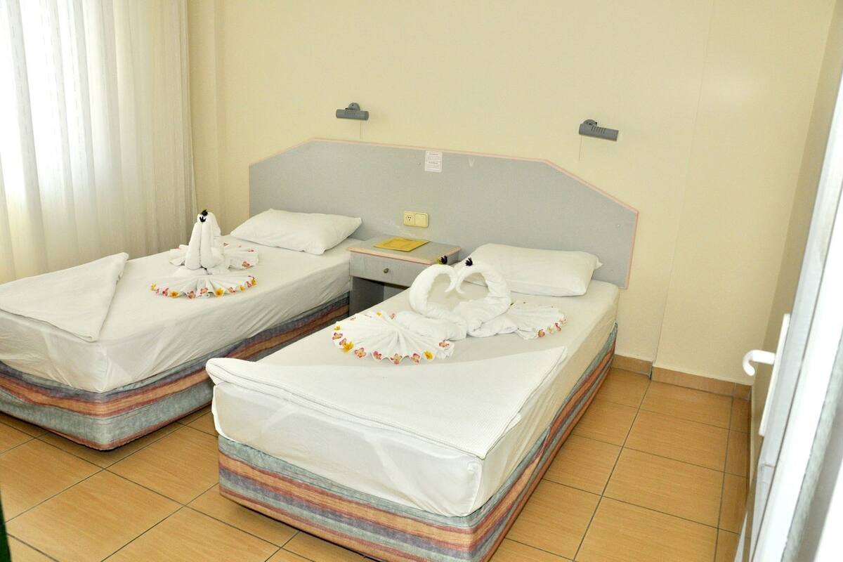 Two twin beds with white linens and decorative swans, a bedside table with a lamp, and a window with curtains.