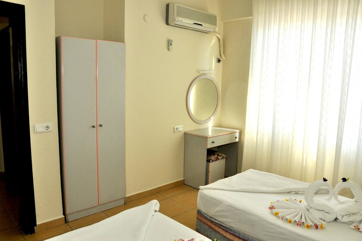 A hotel room with a bed, a wardrobe, a mirror, and a window with curtains.
