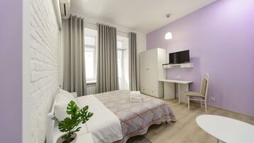 A modern hotel room with a bed, a desk, a chair, a TV, and a potted plant.