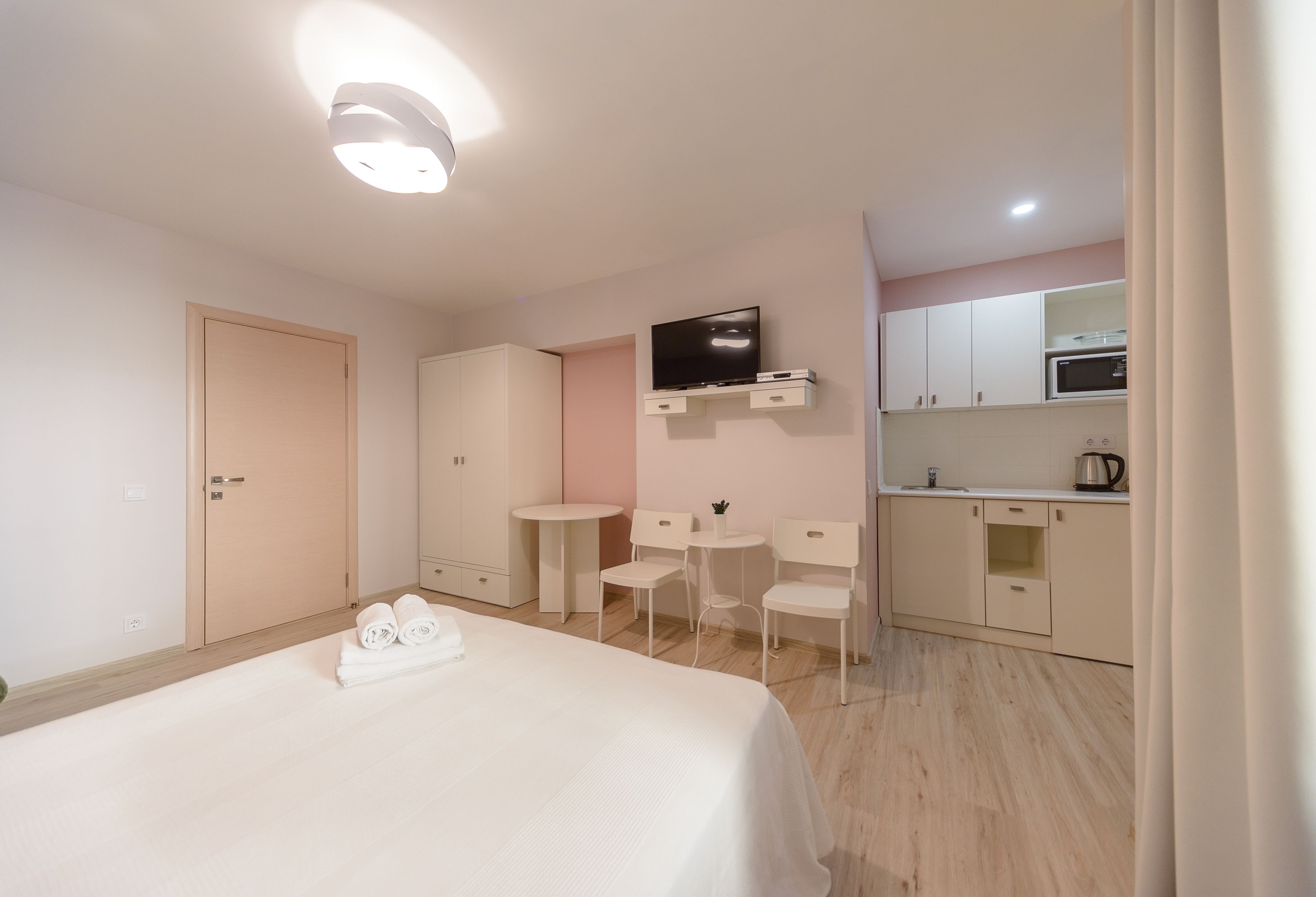 A hotel room with a bed, a small desk, a chair, a television, and a kitchenette.