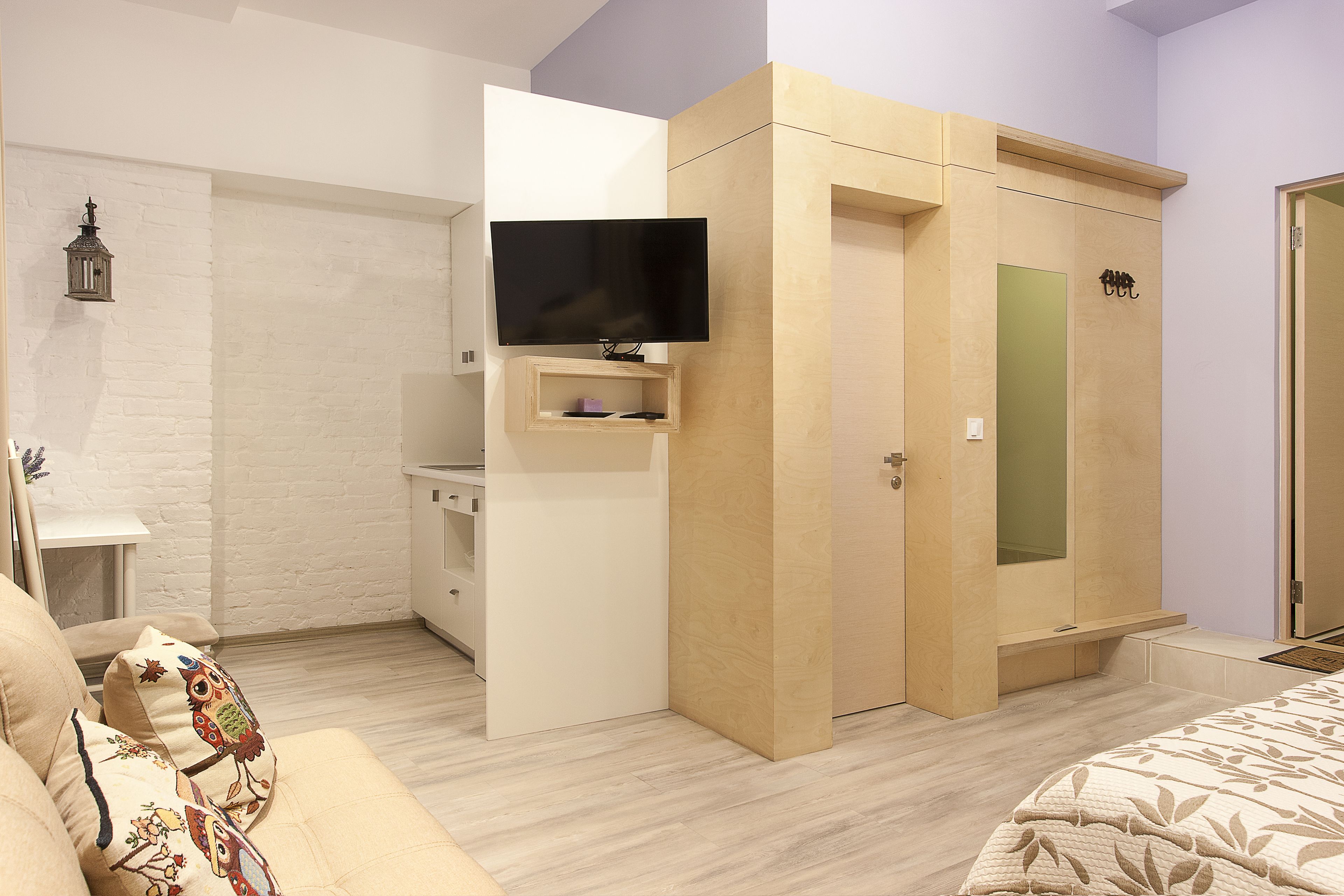 A compact bedroom with a bed, a TV mounted on a wall, a wardrobe, and a small desk.