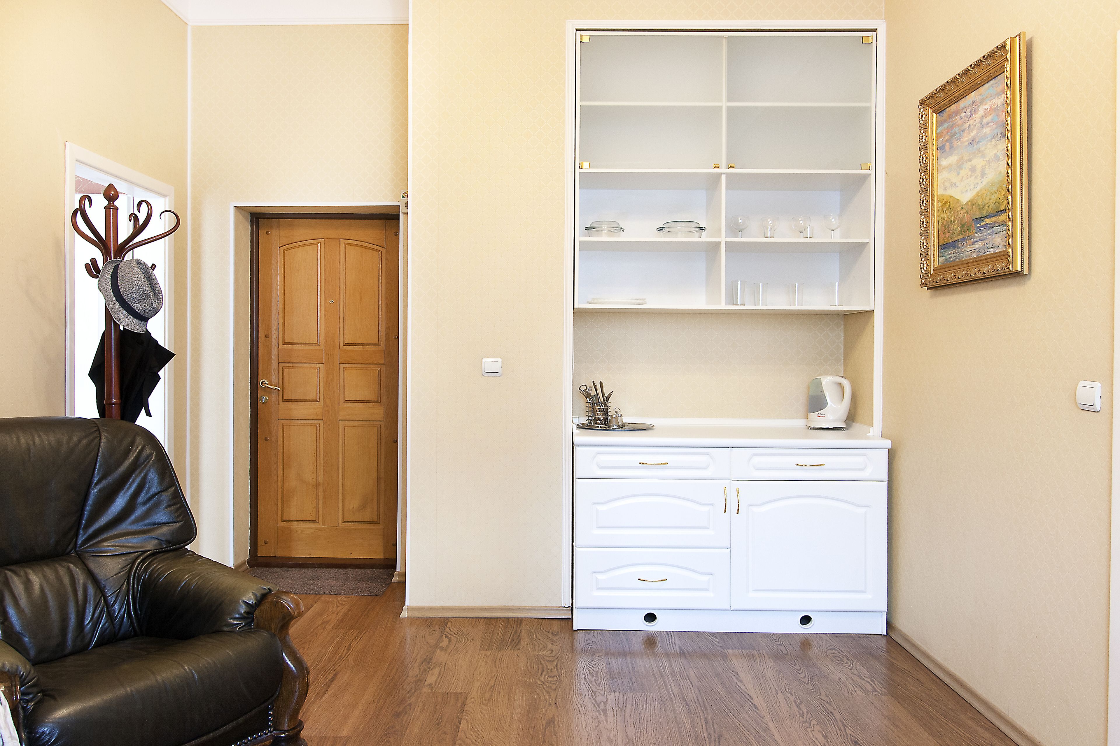 Een kamer met een zwarte lederen stoel, een witte kast met glazen en een houten deur.