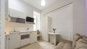A modern kitchen with white cabinetry, a microwave, and a sink. There is a beige sofa and a small round table with a vase. - Centrooms (Kyiv)