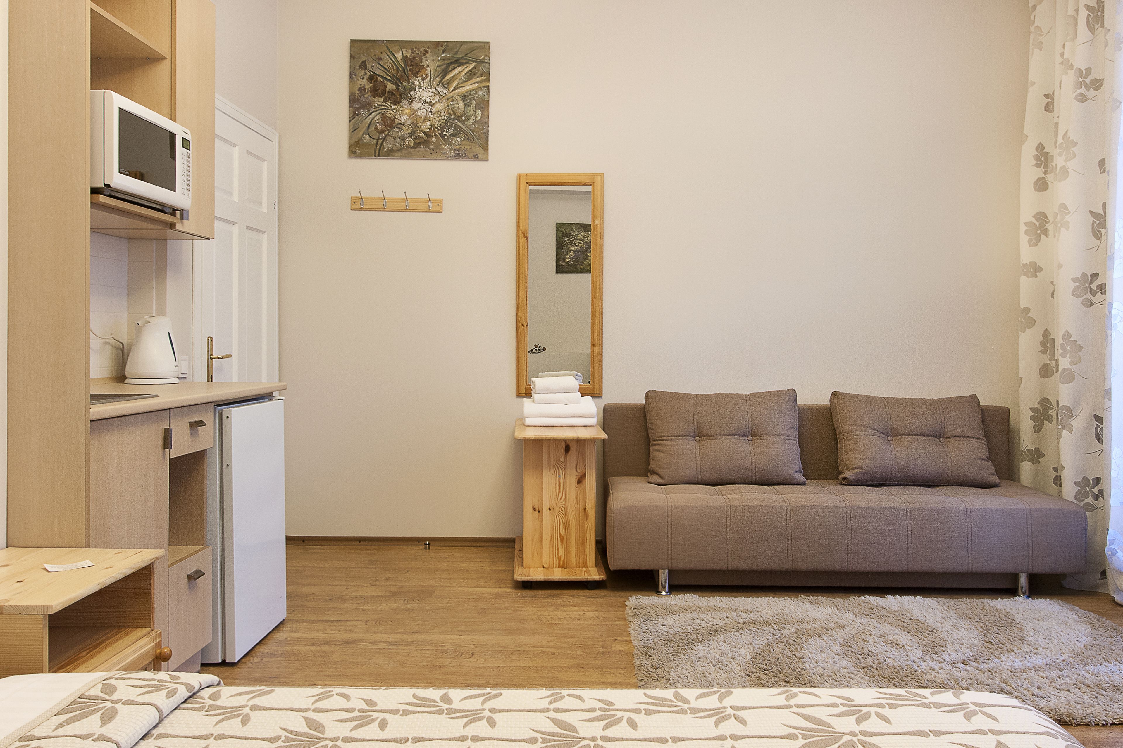 A compact bedroom with a bed, a sofa, a small wooden side table, a microwave, and a mirror.