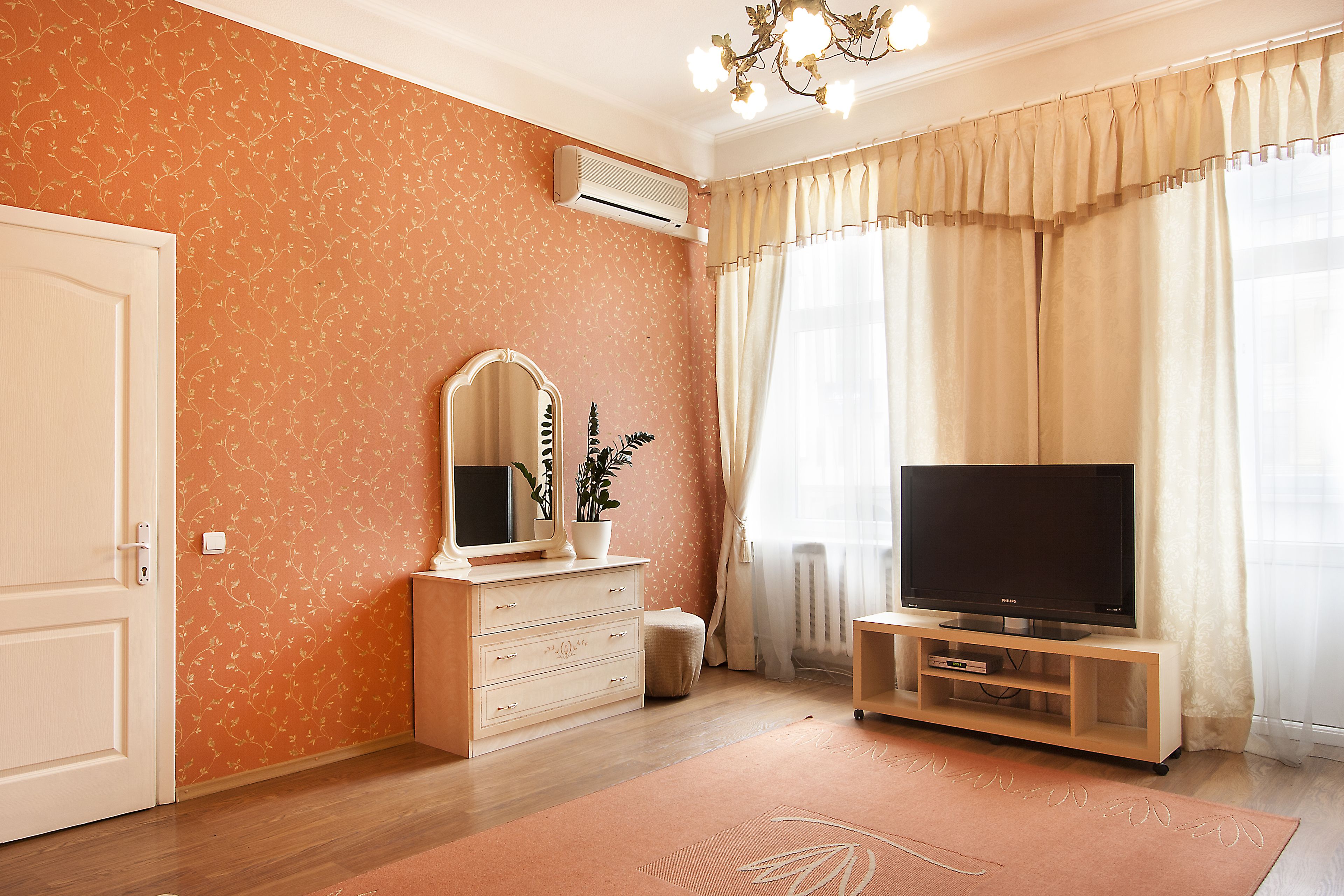A room with a wooden dresser, a television on a stand, a mirror, and a potted plant.