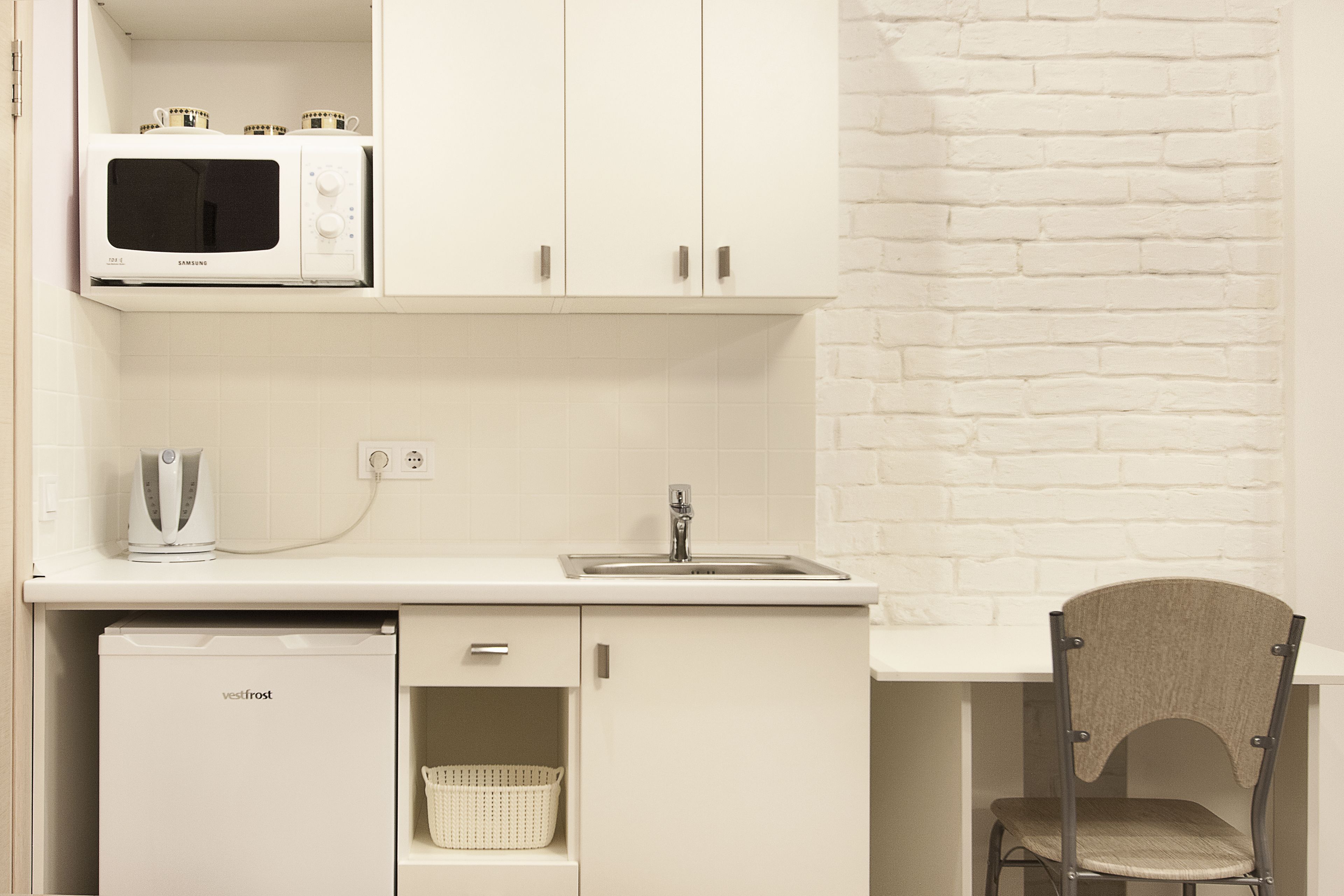 A compact kitchenette with a microwave, a small refrigerator, a sink, and a chair.