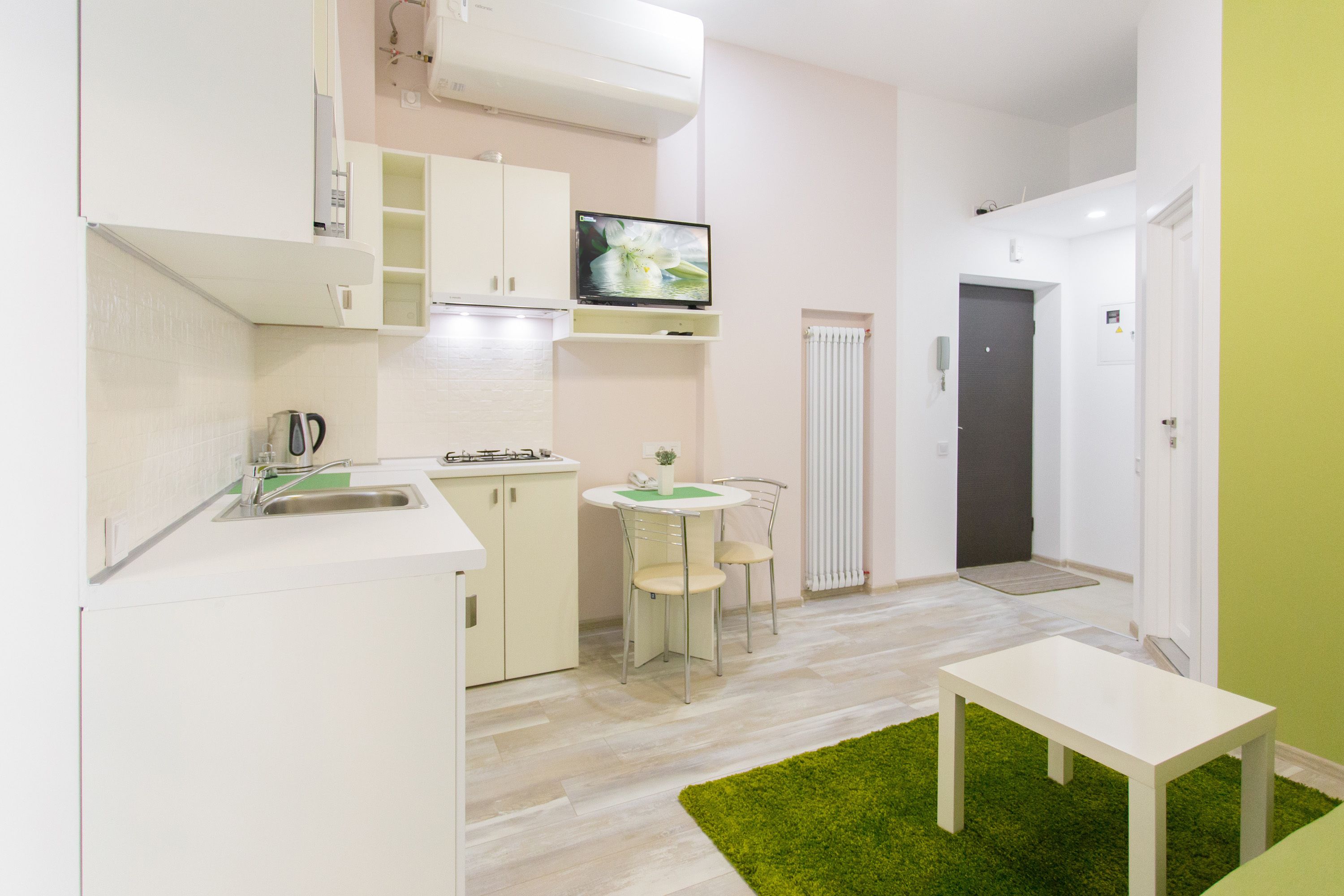 A compact kitchen with a sink, stove, and a television mounted above the counter.