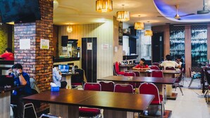 A restaurant with brick walls, wooden tables, and red chairs. - RedDoorz Plus near Mall Panakukang 2 (Makassar)