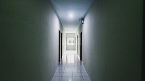 A long, narrow hallway with a tiled floor and light-colored walls. - RedDoorz Plus near Mall Panakukang 2 (Makassar)