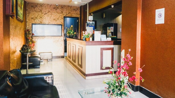 A reception area with a marble wall, a reception desk, a black leather sofa, and a glass table with flowers. - RedDoorz Plus near Mall Panakukang 2 (Makassar)