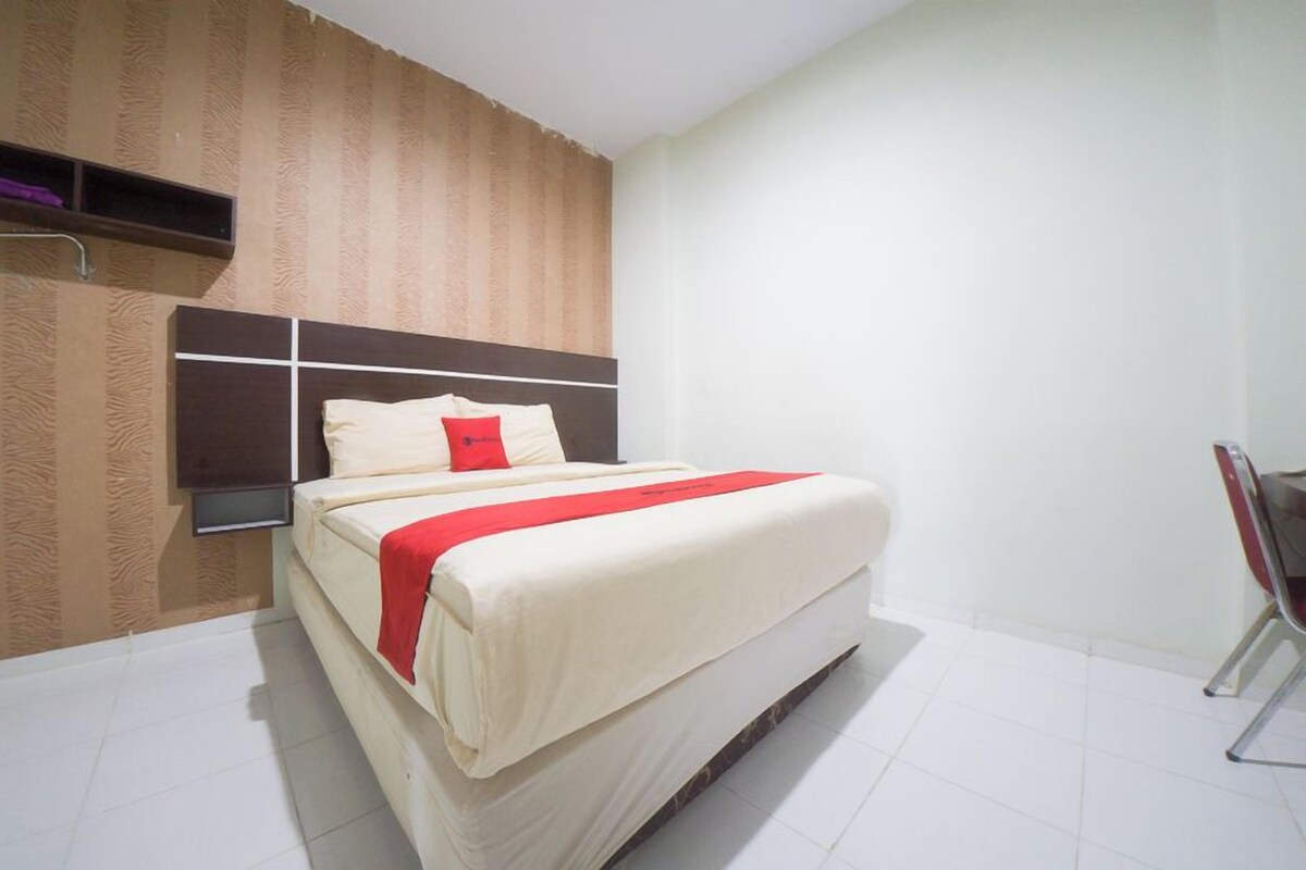 A hotel room with a bed, a nightstand, a wall-mounted shelf, and a chair.