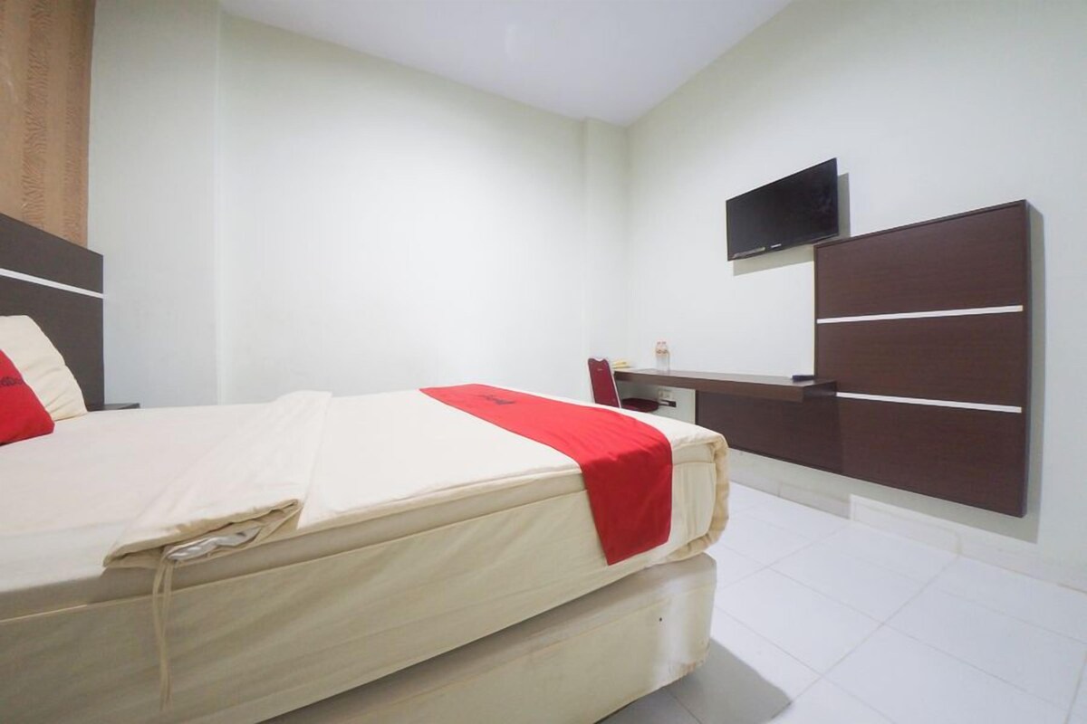 A hotel room with a bed, a desk, and a TV mounted on the wall.