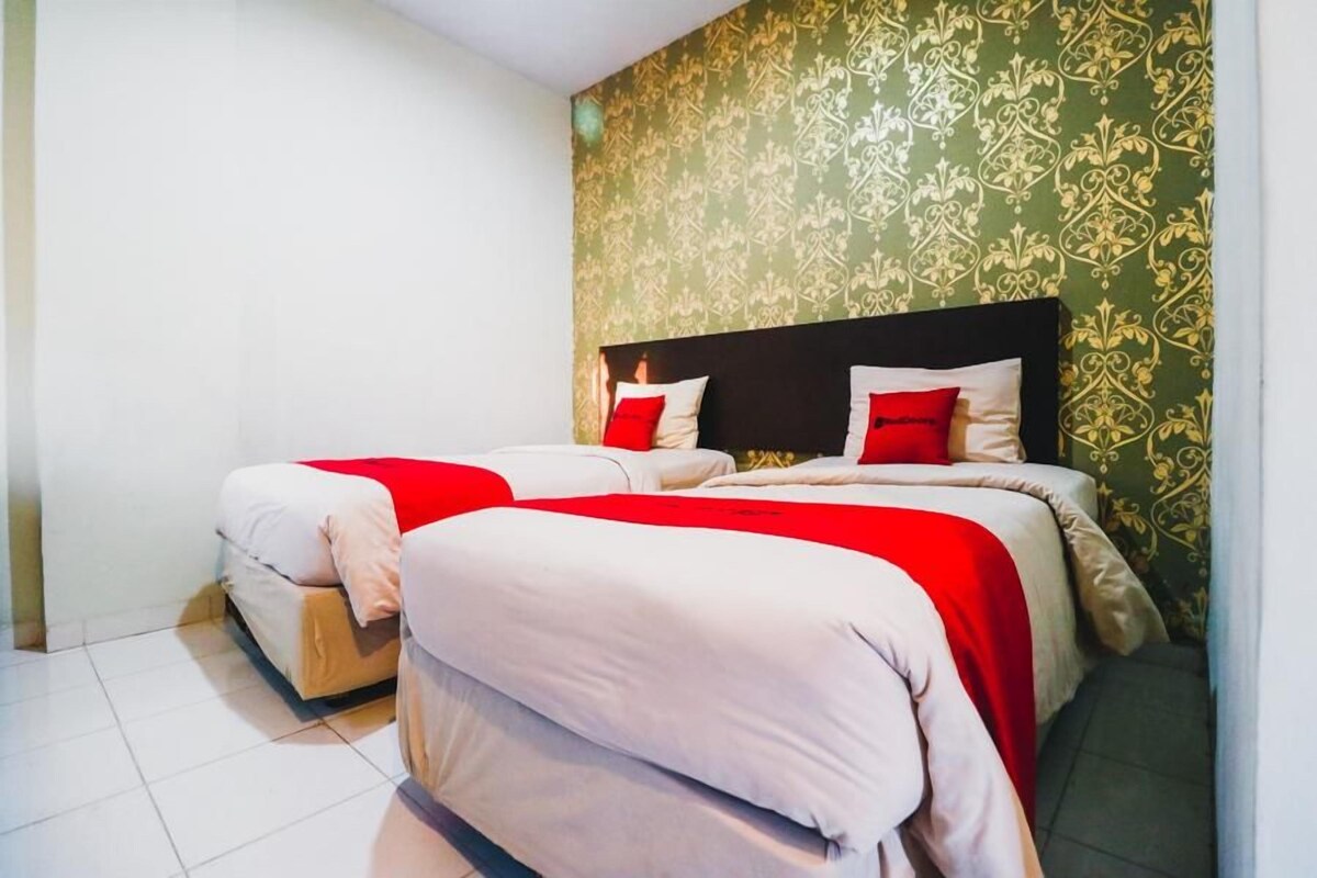 A double bed with red and white bedding, a dark headboard, and a green patterned wall.