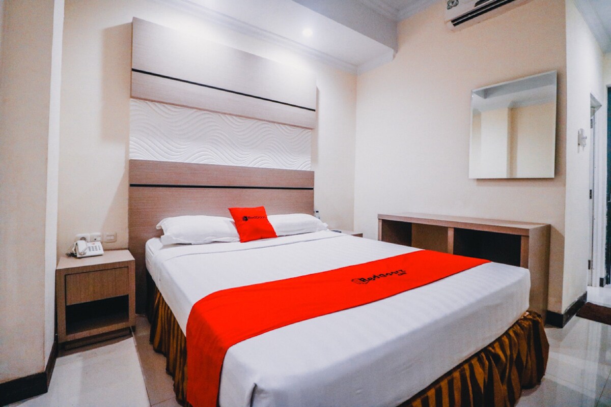 Une chambre d’hôtel avec un grand lit, une table de chevet avec un téléphone, un miroir et une tête de lit en bois.