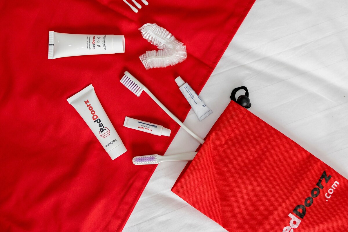 Divers articles de soins personnels, notamment une brosse à dents, du dentifrice et une brosse à cheveux, disposés sur un fond en tissu rouge et blanc.