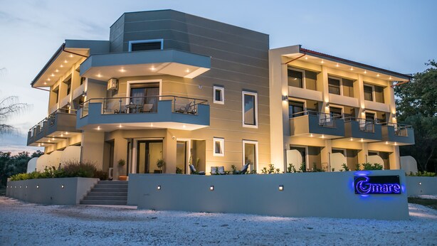 A modern multi-story building with balconies, a well-lit entrance, and a sign that reads "Gmare". - Gmare (Polygyros)