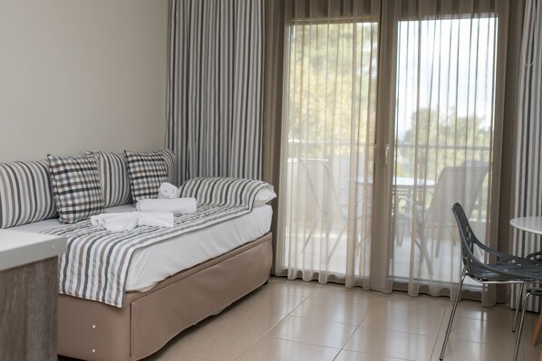Une chambre moderne avec un canapé-lit, des coussins à rayures, un lit parfaitement fait et une vue sur un espace extérieur grâce à de grandes fenêtres.