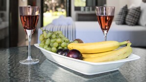 A table with a fruit bowl containing grapes, bananas, and plums, and two glasses of red wine. - Gmare (Polygyros)