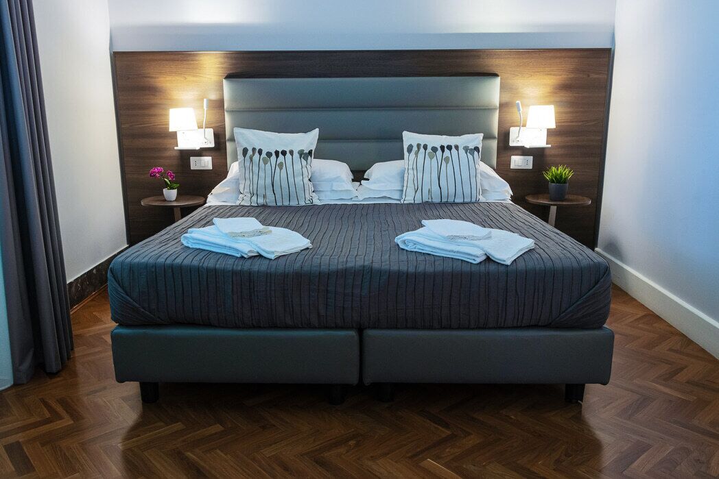 A double bed with a grey upholstered headboard, two bedside tables with lamps, and a wooden floor.