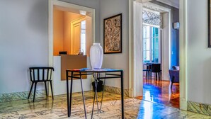 Un pasillo con piso de mármol, un jarrón blanco sobre una mesa y un cuadro abstracto enmarcado en la pared.