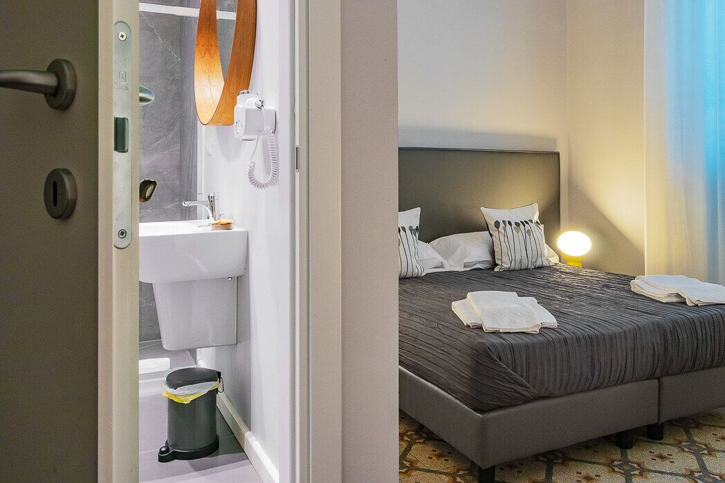 A hotel room with a bed, bedside table, and a bathroom visible through an open door.