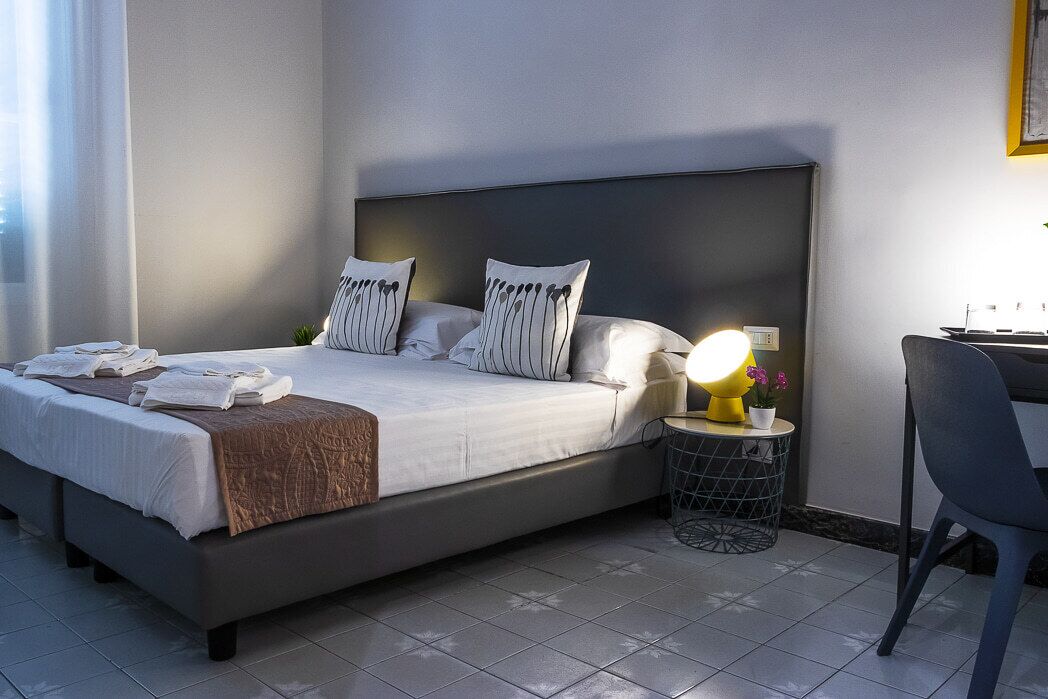 A neatly made bed with pillows, a bedside lamp, and a small table with a plant.