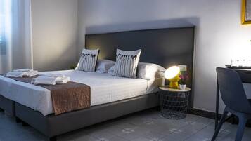 A neatly made bed with pillows, a bedside lamp, and a small table with a plant.