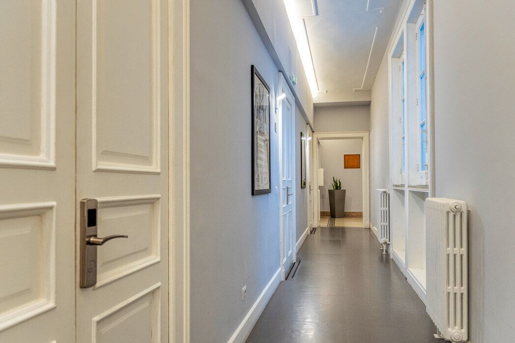 A hallway with white doors, framed pictures on the wall, and a radiator on the right.