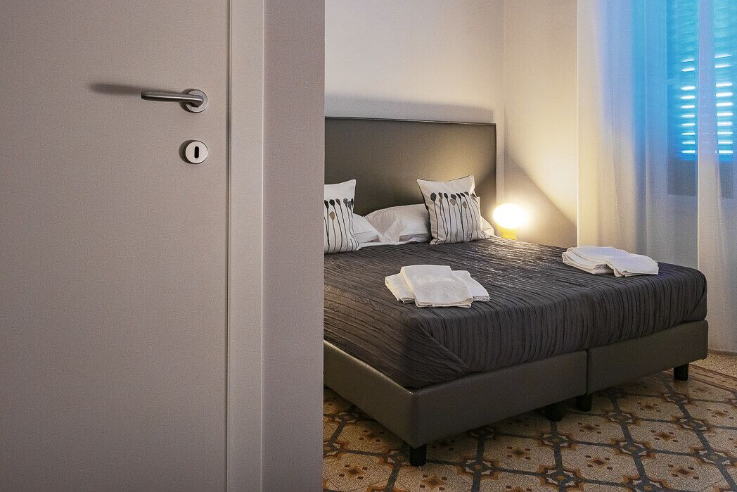 Ein ordentlich bezogenes Bett mit Kissen und einem gefalteten Handtuch, eine Nachttischlampe und ein gemusterter Boden.