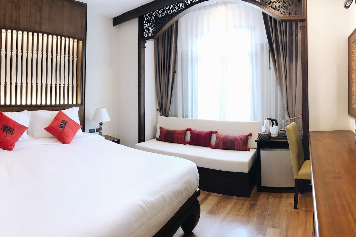A hotel room with a large bed, a seating area, a TV, and a bathroom with a glass shower.