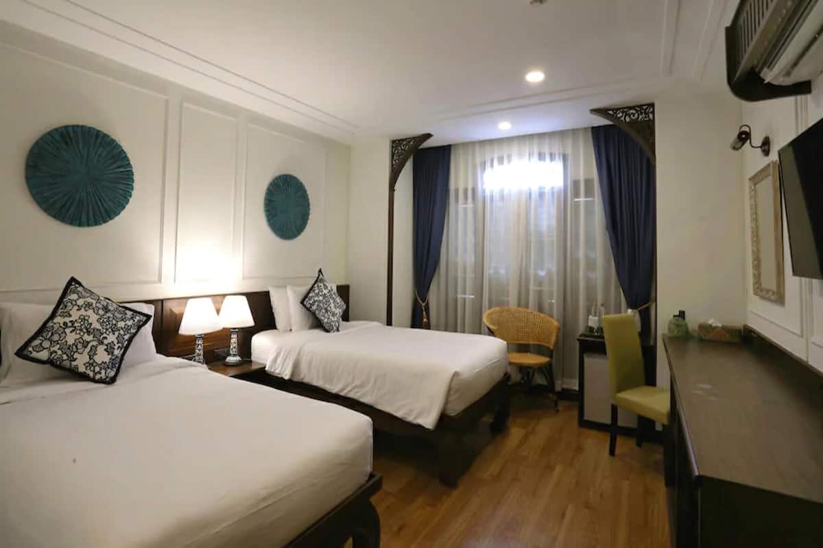 A hotel room with two beds, a desk, a chair, a TV, and a large window with curtains.