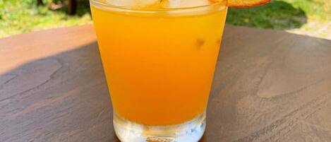 Ein Glas Orangensaft mit Orangenscheibe am Rand, auf einem Holztisch im Freien.