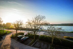A parking area with cars, a pedestrian crossing, and a body of water in the background. - Zum Vater Rhein (Monheim)